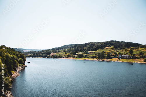 large river surrounded by forest against blue sky, portomarin photo