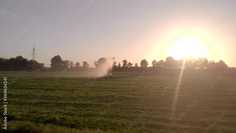 Grassland field approaching a water canon spewing a lot of water keeping the farmland moist during a dry period and heat wave in The Netherlands with the sun behind. Agriculture seasonal concept. Grassland field approaching a water canon spewing a lot of water keeping the farmland moist during a dry period and heat wave in The Netherlands with the sun behind. Agriculture seasonal concept.