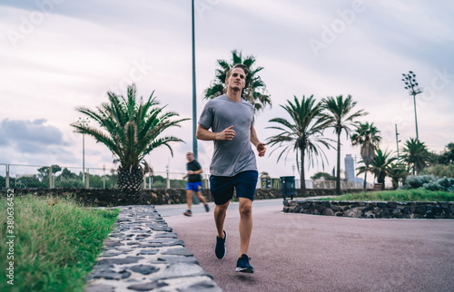 Young active male keeping fit and strong body running on city street in morning enjoying energy and wellness  20s handsome sportsman making warming cardio workout jogging on urban settings