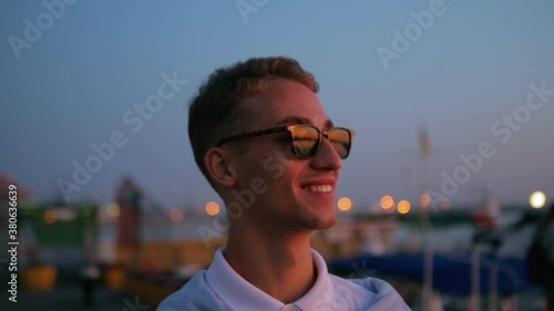 smiling man in black sunglasses wanders along seafront under orange evening sun light slow motion closeup