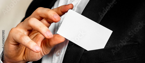 Part of body of man who takes out business card from the pocket of business suit, copyspace. Businessman in black business suit puts white card in pocket. Business concept.
