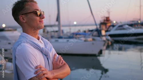 excited guy in black sunglasses stands on seafront edge and breathes fresh air deeply in summer evening slow motion