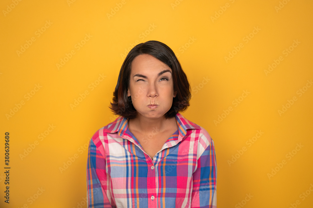Young woman inflated her cheeks on a yellow background in the studio. She has bent her eyebrow and looks up. High quality photo. Young woman inflated her cheeks on a yellow background in the studio. She has bent her eyebrow and looks up. High quality photo.