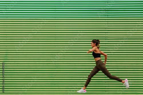runner on the street. girl athlete with sportswear running in front of a green wall