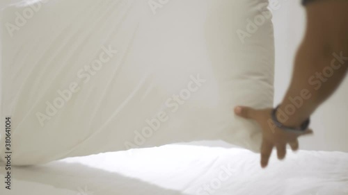 A white pillow is being picked up by a woman who is cleaning the hotel room for the next client.