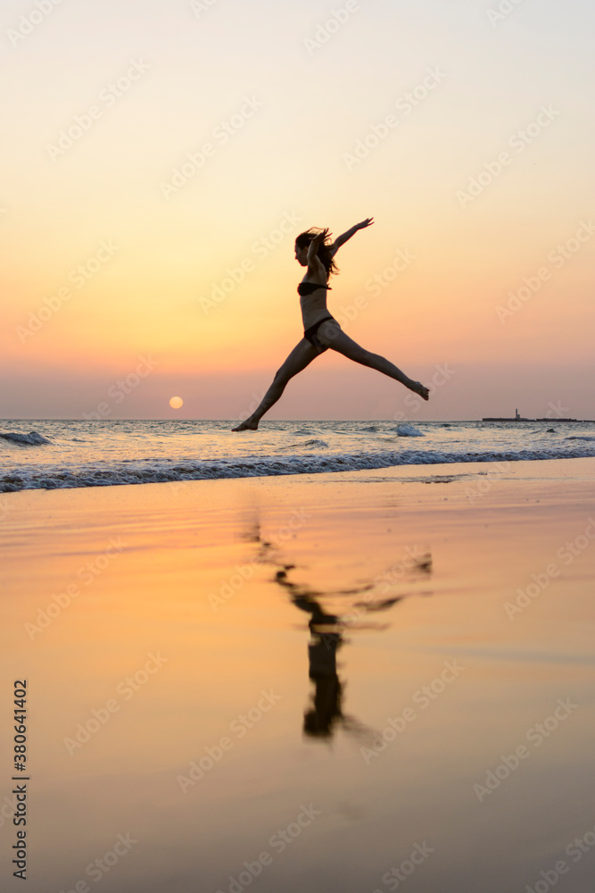 woman jumping on the seashore at sunset