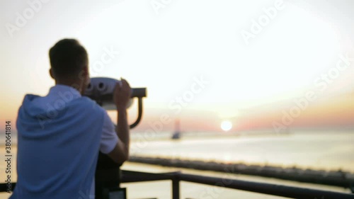 guy in white t-shirt runs to tourist binoculars and admires pictorial summer sunset over endless sea slow motion backside