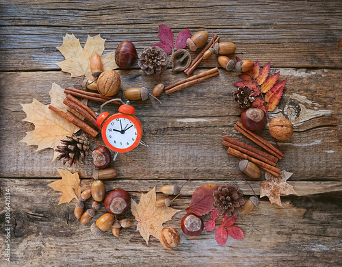 autumn composition. alarm clock, autumnal leaves, acorns, cones, berries on wooden background. autumn time, fall season concept