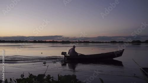 Silhouette of lonely fisherman sailing his boat during blue hour. Static, slomo photo