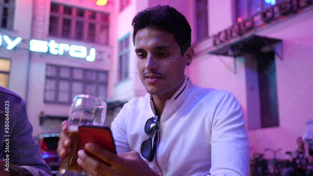 Young Latin Man uses Mobile Smart Phone and drinks a Beer on cozy evening Street Young Latin Man uses Mobile Smart Phone and drinks a Beer on cozy evening Street
