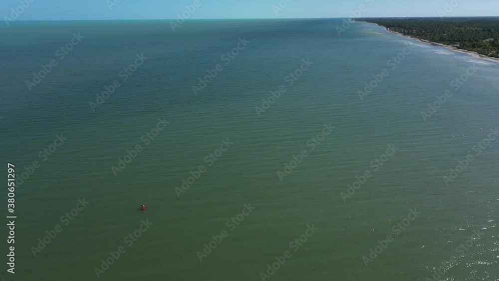 High aerial camera descends showing lone kayaker off a shoreline in warm weather. High aerial camera descends showing lone kayaker off a shoreline in warm weather.