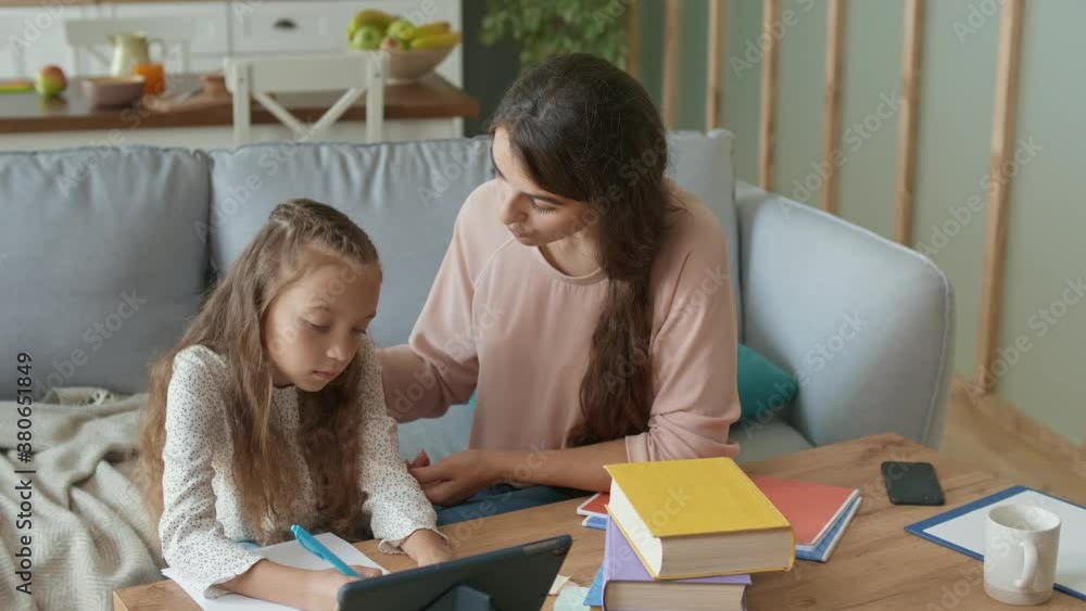 A Lovely Mother Helps to Her Cheerful Daughter Do Homework. Girl Takes a Remotely Education. Doing Homework With a Tablet. A Lovely Mother Helps to Her Cheerful Daughter Do Homework. Girl Takes a Remotely Education. Doing Homework With a Tablet.
