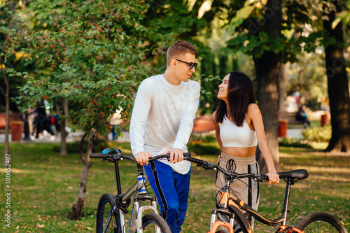 Loving young couple standing in an autumn park with bicycles and talking with a smile on their faces. Leisure on bicycles autumn season