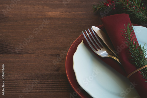 Traditional Christmas table setting. Silverware, red linen napkin, plates and fir branches on wooden table. Winter holidays background. Сopy space, close up