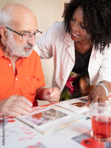 African American medical assistant watching a photo album with an ederly man