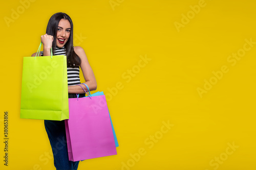Smiling woman holding shopping bags, isolated on yellow background with space for text