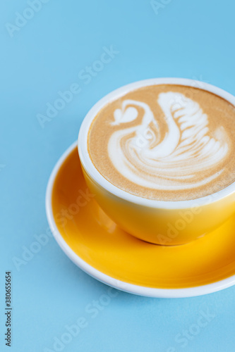 Yellow cup with cappuccino on blue wooden background