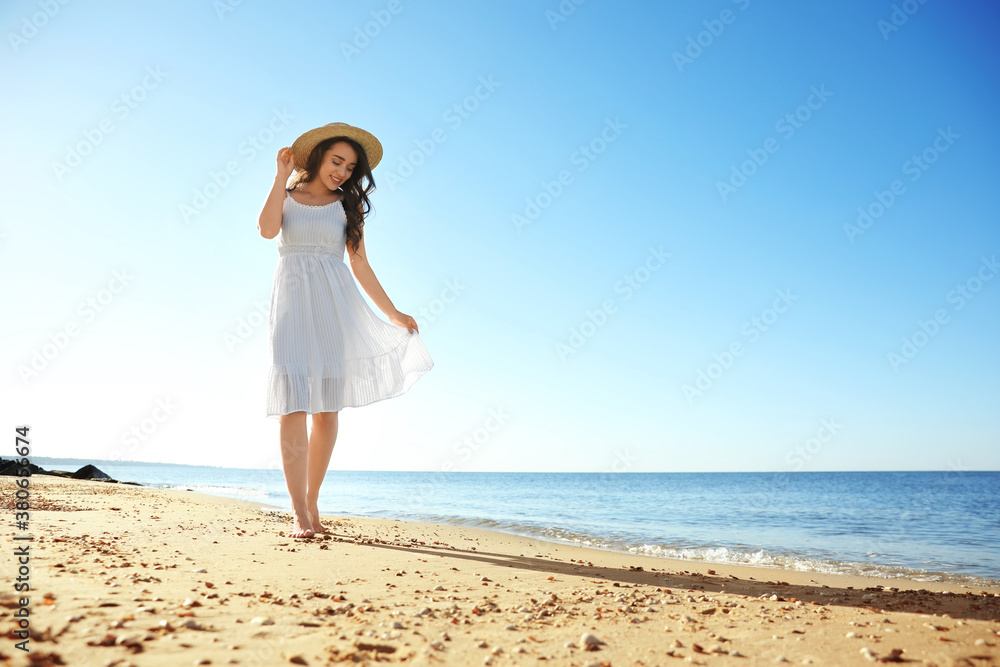 Happy young woman with hat walking on beach near sea. Space for text Happy young woman with hat walking on beach near sea. Space for text