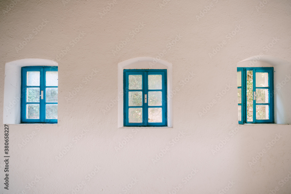 Inside view of three blue windows on a white wall.