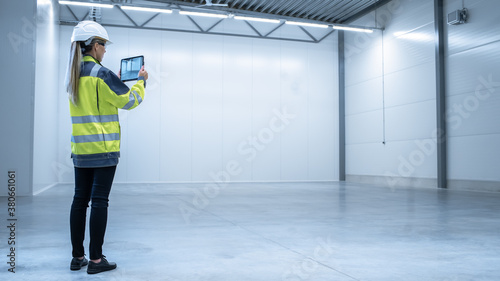 Industry 4.0 Modern Factory: Female Engineer is Stanging in Empty Warehouse and Using Digital Tablet Computer with Augmented Reality Software for Mapping Manufacturing Plant Room, Factory Layout.