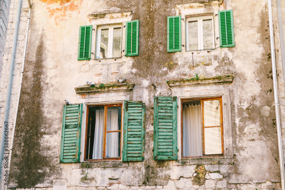 An old multi-storey building with windows and wooden shutters with peeled paint.