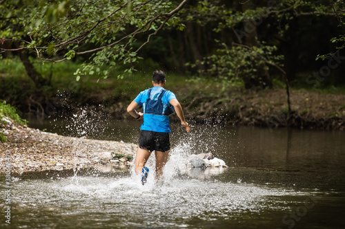 Young man in sports equipment running in mountain river