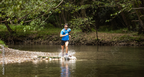 Young man in sports equipment running in mountain river