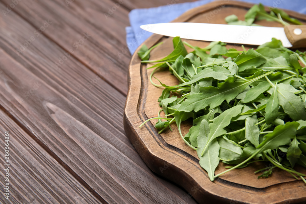 Cutting board with fresh arugula leaves and knife on wooden table, closeup. Space for text Cutting board with fresh arugula leaves and knife on wooden table, closeup. Space for text