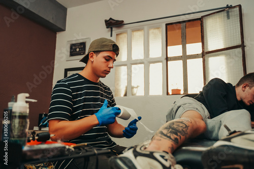 Young tattoo artist picking up roll of paper in a tattoo studio.