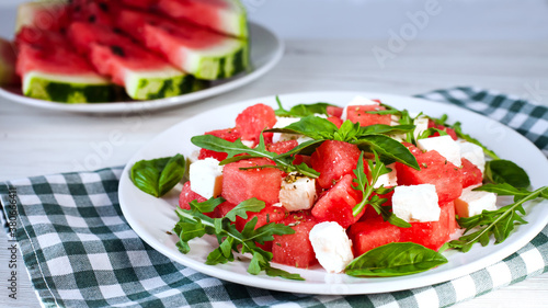 Fresh delicious juicy salad with watermelon, feta cheese, arugula and basil leaves on white plate. Close-up. Side view. Healthy food concept.