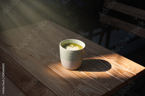 A cup of green tea matcha latte on wooden table at cafe. Healthy food concept. Sun rays. Side view. Close-up.