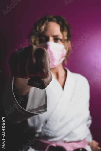 Powerful woman during the coronavirus crisis karate pose giving a punch. Pink background with shadows