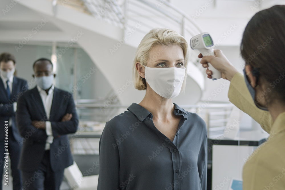 Business executives having temperature checked at reception of office Business executives having temperature checked at reception of office