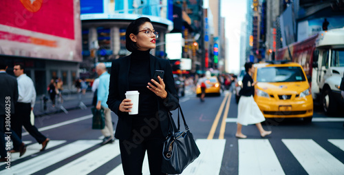 Stylish woman in suit standing on crosswalk with coffee
