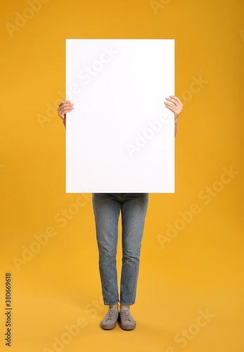 Woman holding white blank poster on yellow background. Mockup for design