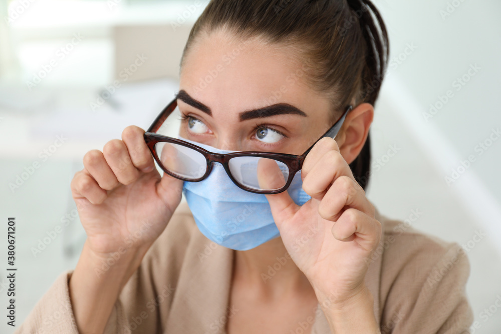 Woman wiping foggy glasses caused by wearing medical mask indoors, closeup Woman wiping foggy glasses caused by wearing medical mask indoors, closeup