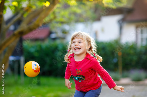 Little adorable toddler girl playing with ball outdoors. Happy smiling child catching and throwing, laughing and making sports. Active leisure with children and kids.