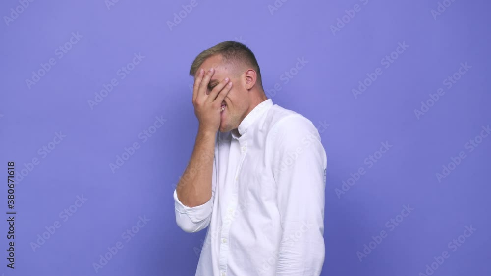 Young caucasian man blink at the camera through fingers, embarrassed covering face Young caucasian man blink at the camera through fingers, embarrassed covering face