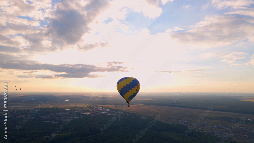 Aerial drone view of colorful hot air balloon flying over green park in small european city at summer sunset