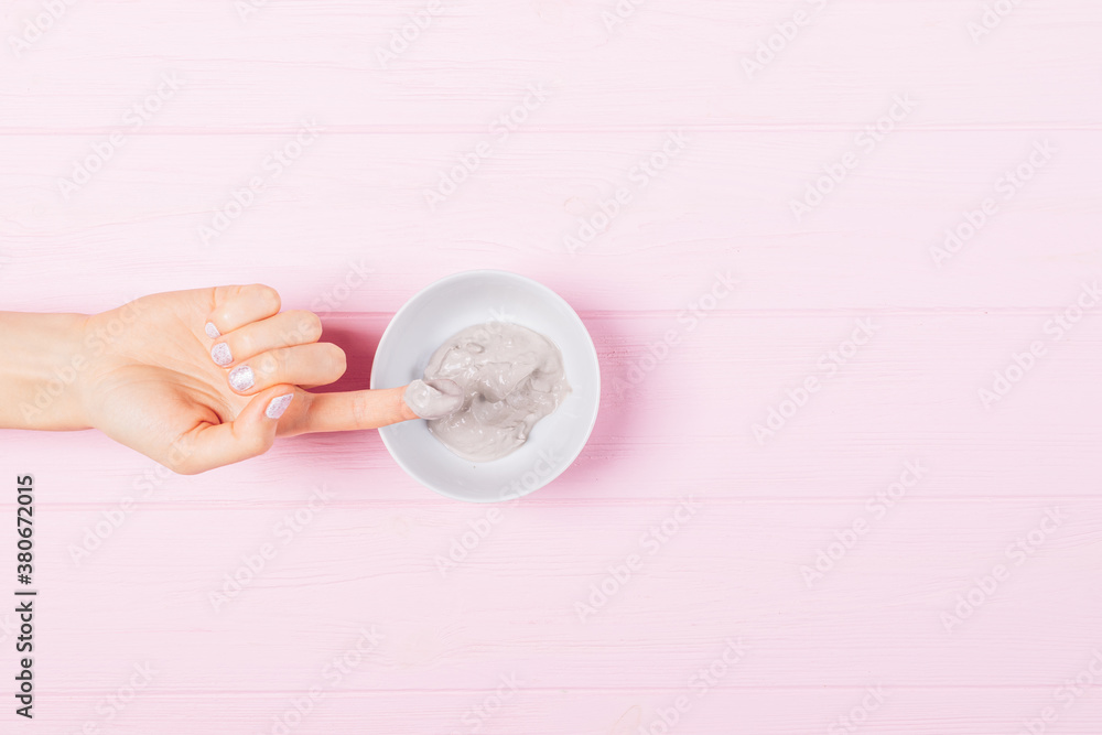 Female hand takes sample of clay facial mask from bowl Female hand takes sample of clay facial mask from bowl