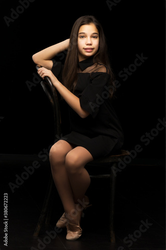 Portrait of a little girl sitting on an old Viennese chair, black background. © lotosfoto