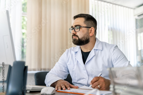 Man sitting at desk. Doctor in scrubs at office near computer. Office in hospital.