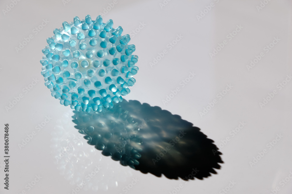 Bright blue transparent massage ball lying in the sun on a plain white background and looking like a virus. Seen in Germany in September. Bright blue transparent massage ball lying in the sun on a plain white background and looking like a virus. Seen in Germany in September.