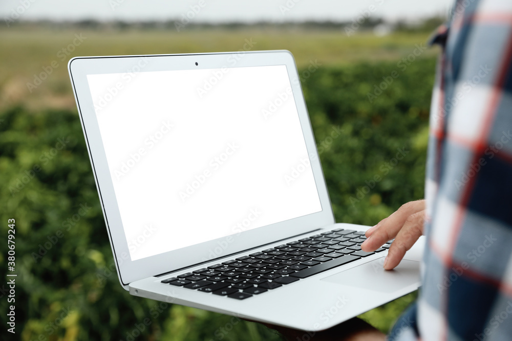 © New Africa - Man using laptop with blank screen in field, closeup. Agriculture technology