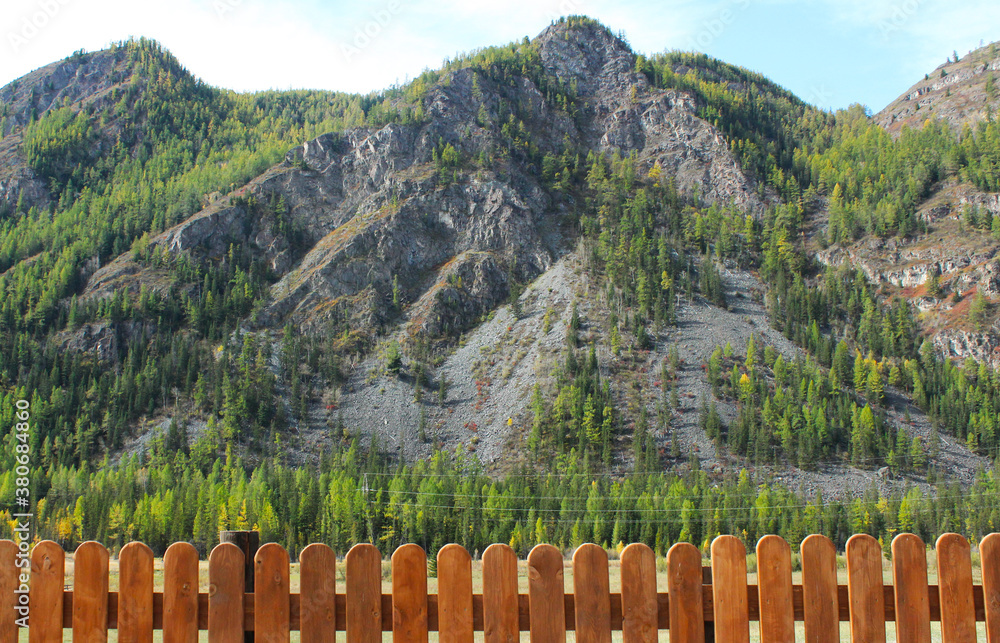 High mountains with trees behind a wooden fence