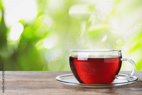 Glass cup of fresh hot tea on wooden table against blurred green background. Space for text