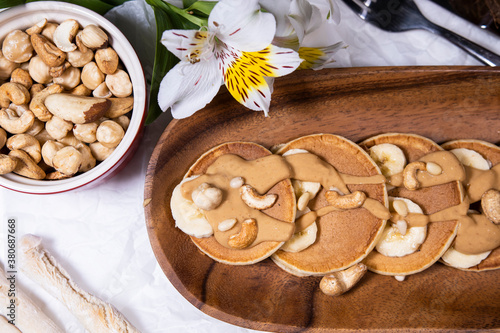 Pancakes with mix of nuts and peanut butter on white background with flowers. Trendy food.