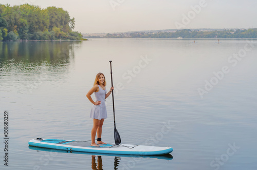 Young woman in a dress swims on the lake on a surfboard