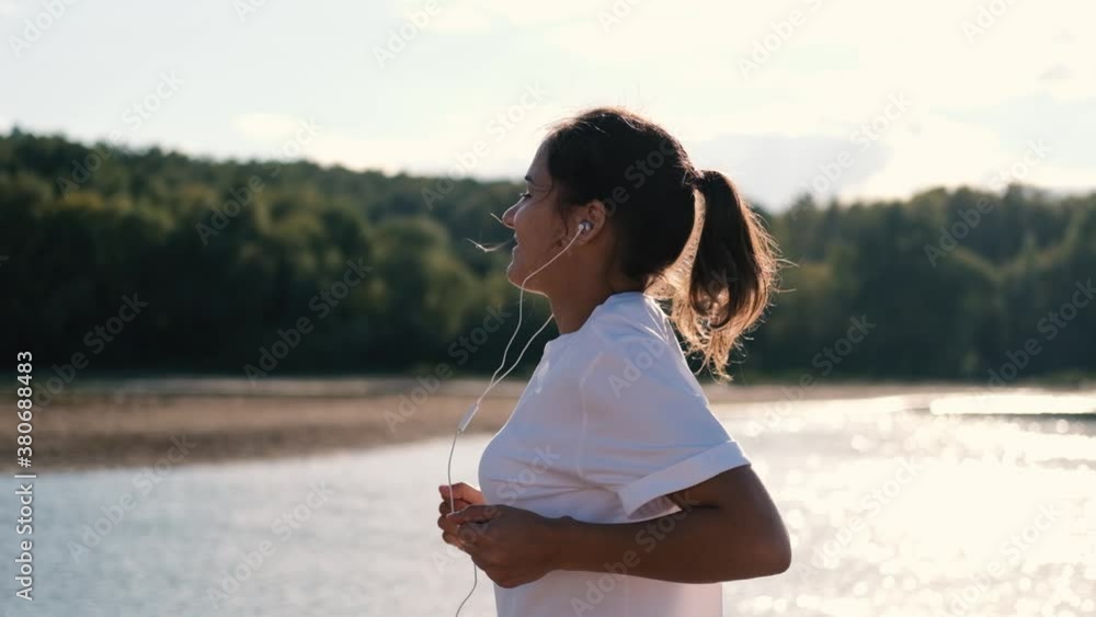 A woman in headphones runs at a beautiful sunset on the beach, sun glare from the water. Sport and healthy lifestyle concept A woman in headphones runs at a beautiful sunset on the beach, sun glare from the water. Sport and healthy lifestyle concept