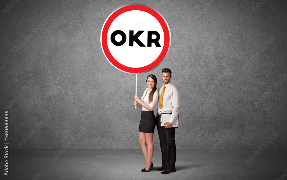 Young business person holdig traffic sign with OKR abbreviation, technology solution concept Young business person holdig traffic sign with OKR abbreviation, technology solution concept